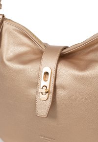 Gouden leren handtas met een gestructureerde afwerking, voorzien van een ritssluiting en een opvallende goudkleurige sluitaccent op de band.