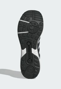 Suela de zapatilla deportiva en blanco y negro que presenta una superficie de goma texturizada, con surcos prominentes y un elemento de torsión central para soporte.