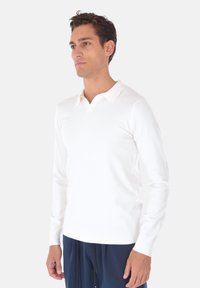 Maglione polo bianco a maniche lunghe con scollatura a V e una trama morbida e liscia. Design semplice con polsini e orlo a coste. Stile minimalista.