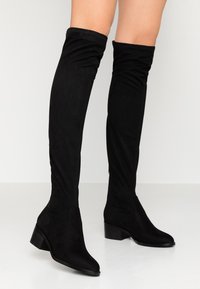 Black over-the-knee boots made of soft suede, featuring a fitted design, pointed toe, and stacked heel for added height.