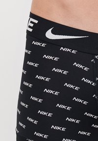 Schwarze Nike Boxershorts mit einem sich wiederholenden weißen Logomuster, glatter Textur und einem weißen elastischen Bund mit Logo.