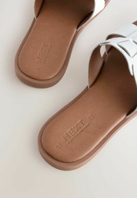 Sandales blanches avec un motif en croix ; semelle texturée marron avec le logo en relief "NEXT" et "FOREVER COMFORT".
