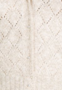 Kremowa dzianina z wzorem diamentowym i guziczkami przypominającymi perły wzdłuż centralnego szwu.