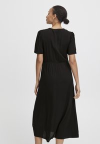 Vestido negro midi con mangas cortas abullonadas, cintura entallada, textura suave y tela fluida, mostrado desde atrás.
