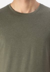 Olivgrünes Baumwoll-T-Shirt mit rundem Ausschnitt, kurzen Ärmeln und glatter Textur. Keine sichtbaren Muster oder Hardware-Details.