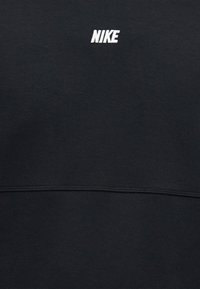 Μαύρο ύφασμα με μικρό λευκό λογότυπο Nike κεντημένο στο πάνω κέντρο και ορατή οριζόντια ραφή κάτω από το λογότυπο.