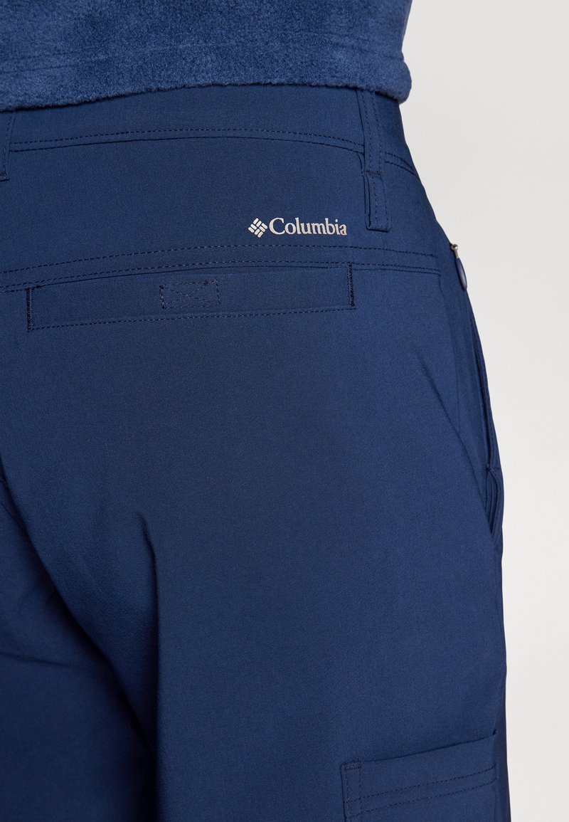 Pantalons d'extérieur bleu marine en tissu doux, dotés d'une poche arrière et du logo Columbia, avec une texture lisse et un design ajusté.