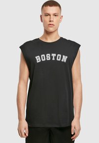 Juodas be rankovių marškinėliai, kuriuose baltais rašmenimis užrašyta "BOSTON", su raukšlėtu paviršiumi, apvaliu kaklu ir laisvu siluetu.