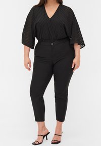 Svart randig overlay-topp med djup V-ringning, parat med figursydda svarta byxor. Har breda ärmar och hög midja. Accenteras med svarta sandaler.