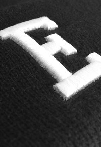 Svart stoff med hvite broderte bokstaver "EH" med en teksturert finish, som fremhever kontrasten mellom materialene.