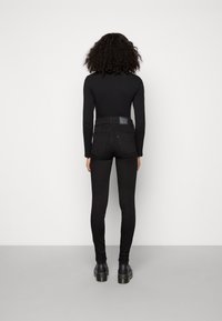 Černé džínové kalhoty s vysokým pasem a slim fit, s minimálním zdobením a s logem na zadní straně. Komplet doplněný černými kotníkovými botami.