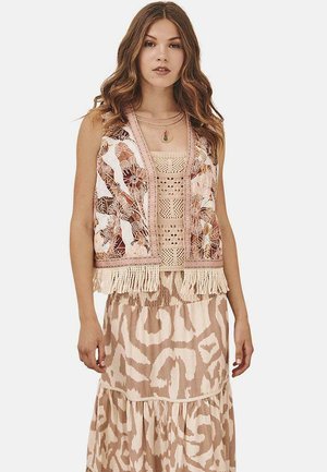 Chaleco bordado con diseño floral, con flecos en el dobladillo, superpuesto sobre un top de ganchillo beige y una falda fluida y estampada en tonos neutros.