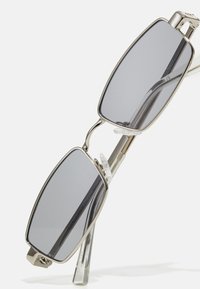 Lunettes de soleil rectangulaires avec des verres gris, monture en métal, embouts de branche transparents et accents au niveau du nez. Design minimaliste avec une finition polie.