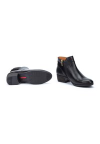 Bottes noires en cuir jusqu'à la cheville avec un bout rond, une fermeture éclair sur le côté et un talon empilé. Texture lisse avec un design minimaliste et un accent rouge contrastant sur la semelle.