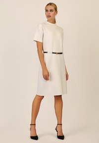 Weißes, kurzärmeliges Kleid mit geradem Schnitt, ausgestattet mit einem schwarzen Gürtel mit goldener Akzentuierung in der Taille. Glatte, strukturierte Stoffqualität.