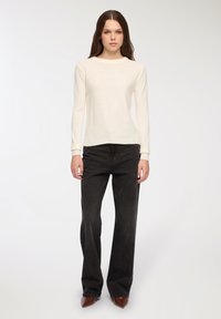 Kremowy sweter robiony na drutach z długimi rękawami, okrągłym dekoltem i ściągaczami, zestawiony z czarnymi spodniami o szerokich nogawkach i brązowymi szpilkami w szpic.