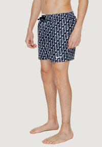 Pantaloni da nuoto blu con motivo a onde bianche, fascia elastica in vita con coulisse, taglio fino al ginocchio e texture del tessuto liscia.
