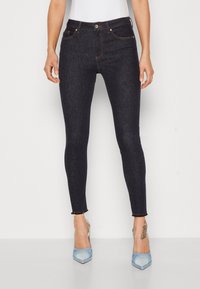 Jeans ajustados de color azul oscuro hechos de mezclilla, con una cintura a media altura, costuras naranjas y un dobladillo sin acabar en el tobillo.