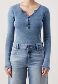 Långärmad, blå ribbad henley-top med treknappslå; parat med ljustvättade denimjeans med lätt slitage och framfickor.