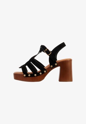 Sandale noire à brides avec clous dorés, boucle de cheville ajustable et talon bloc en bois marron épais.