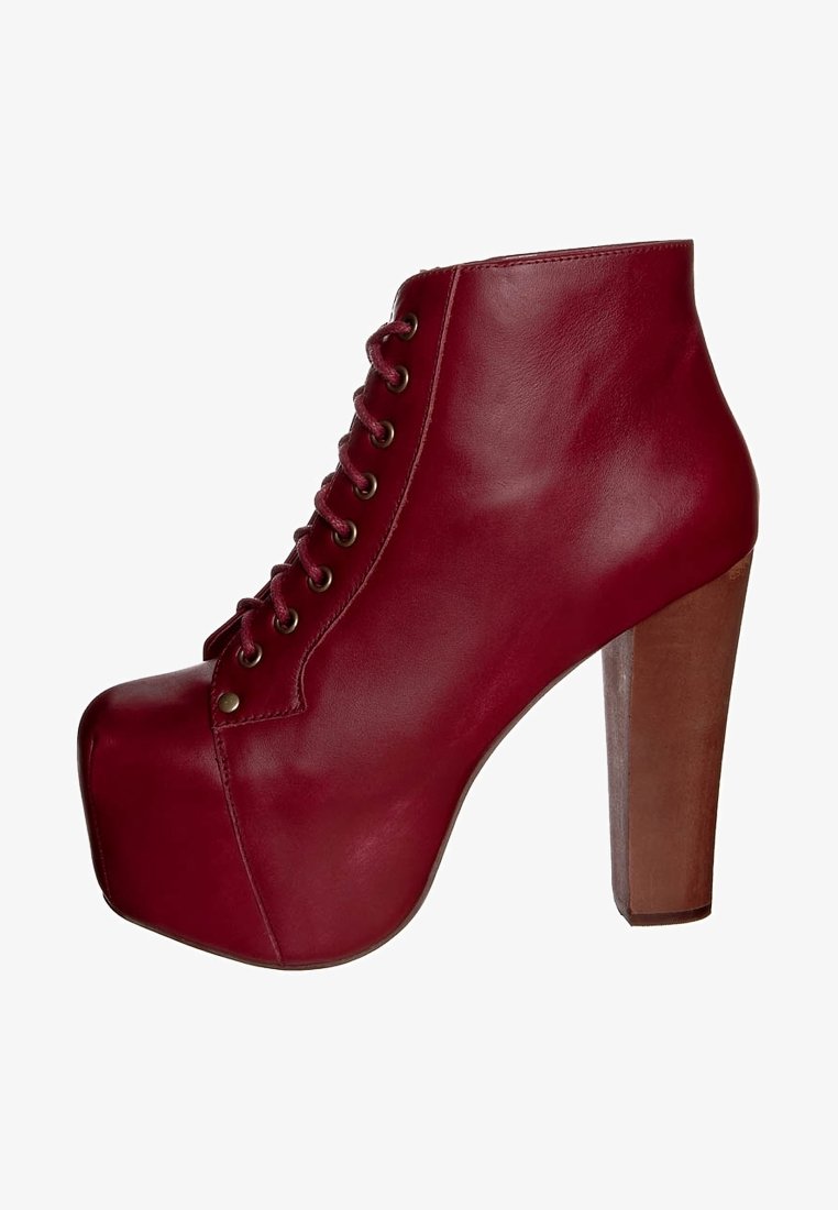 Rode leren enkelboot met een hoge, chunky hak en platform, voorzien van een vetersluiting en een ronde neus. Soepele textuur met minimale accenten.