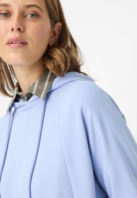 Felpa con cappuccio azzurro chiaro con coulisse, colletto a righe verdi e bianche a contrasto e tessuto morbido e liscio.