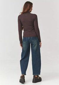 Brązowy dopasowany sweter w serek noszony z niebieskimi, wysokimi, luźnymi dżinsami. Czarne buty na platformie dopełniają outfit.