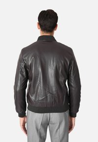 Giubbotto bomber in pelle nera con colletto e polsini a coste, dal design leggermente aderente e con variazioni di texture ben visibili.