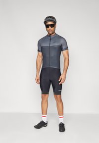 Îmbrăcăminte de ciclism cu un tricou scurt, gri și pantaloni scurți negri. Prezintă un fermoar frontal, logo-ul Giro și este concepută pentru performanță. Pantofi de ciclism negri și cască.