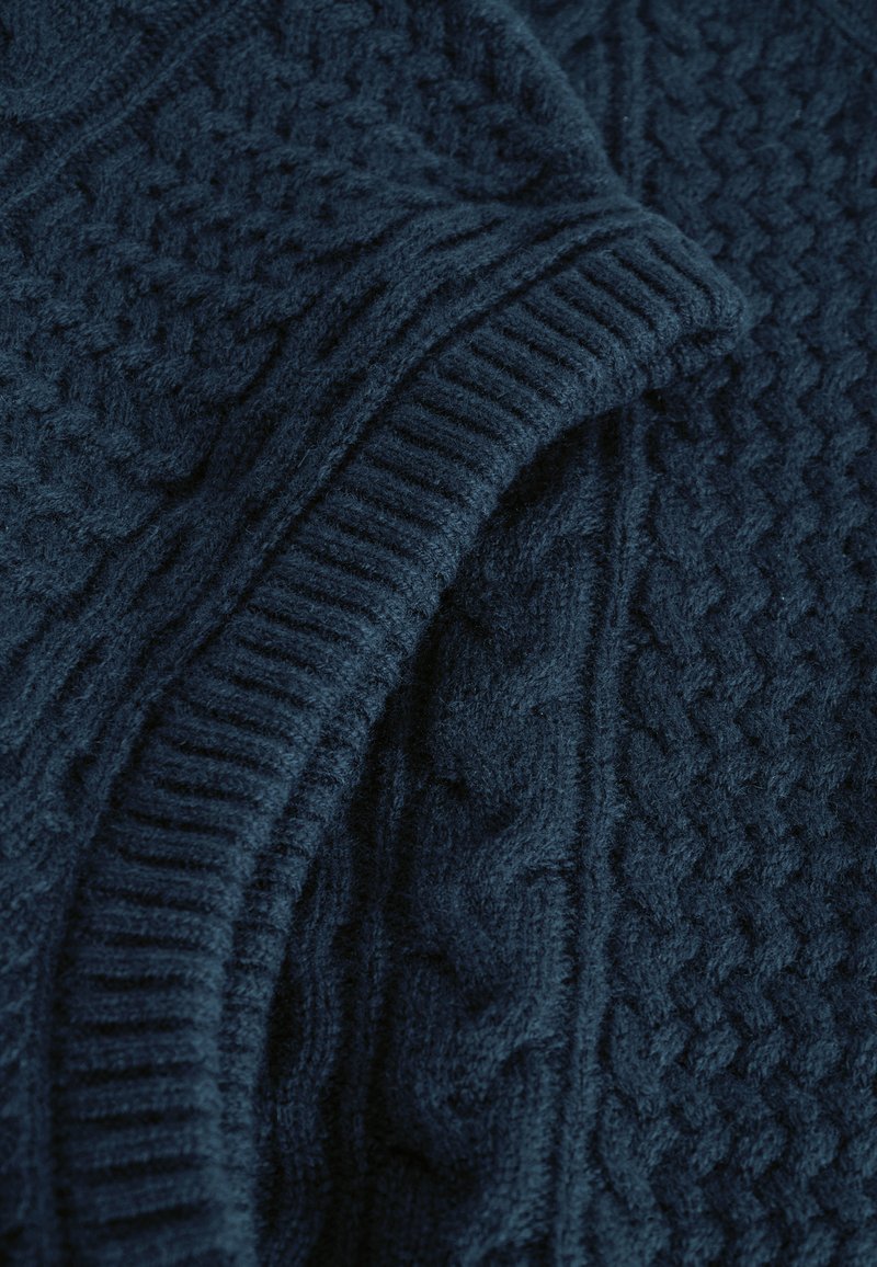 Pull en tricot bleu marine avec des motifs en relief et des poignets côtelés. Matière douce et pelucheuse avec des détails complexes sur le tissu.