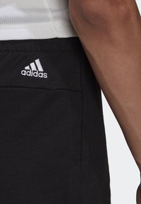Svarta atletiska joggingbyxor med en sidficka, prydda med en vit broderad Adidas-logotyp. Tillverkade av mjukt, texturerat bomullsmaterial.