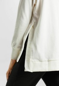 Sudadera color crema con aberturas laterales, puños acanalados y sutiles letras "SPORT". Fabricada con una tela suave, tiene un corte relajado.