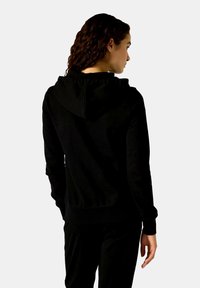 Schwarzer Baumwoll-Hoodie mit einer Kapuze mit Kordelzug, gerippten Bündchen und Saum sowie einem lockeren Schnitt. Von hinten getragen, mit einer glatten Textur.