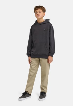 Felpa grigia con cappuccio e tasca frontale, indossata con pantaloni beige e scarpe da ginnastica grigie. Logo stampato sull'area del petto sinistro.