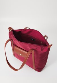 Maroon tote bag made of nylon with brown leather accents. Features a zipper closure and an interior pocket with a gold button detail.