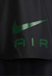 Logo Nike Swoosh vert et le mot "AIR" imprimés sur la partie inférieure d'un vêtement noir.