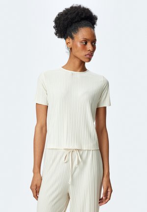 Haut crème à manches courtes en côte avec un col rond. Présente une coupe décontractée et un tissu doux et texturé. Assorti à un pantalon à cordon de serrage.
