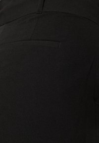 Pantalon noir en tissu lisse, présentant une texture subtile avec une seule poche arrière et des lignes épurées pour un look sur mesure.