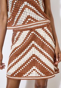 Conjunto de ganchillo en marrón y blanco que presenta una parte superior de diseño con motivos en zigzag y diamantes, acentuada con una banda sólida en el dobladillo.