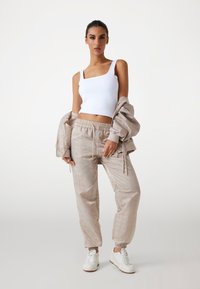 Casual outfit featuring a white tank top, beige patterned joggers with elastic cuffs, and white sneakers. Light fabric and a relaxed fit.