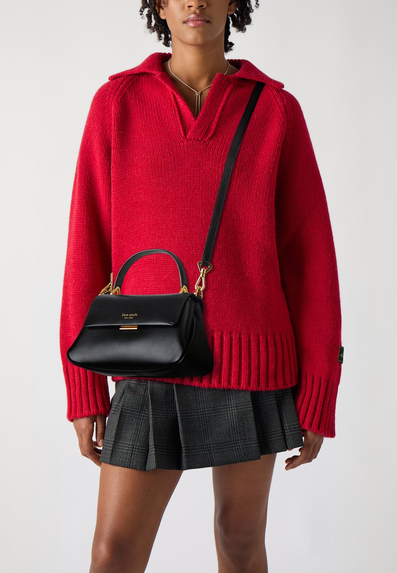 Maglione rosso a maglia con scollo a V e orlo a coste, abbinato a una borsa in pelle nera con manico superiore e dettagli in metallo dorato.