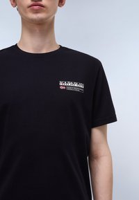 Svart bomull t-shirt med rund hals, korta ärmar och en liten framsida logotyp i vit och röd text med en flaggaccent.