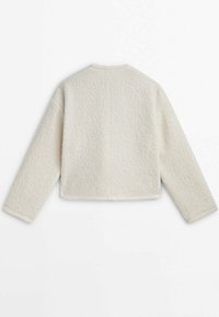 Jasno-beżowa, krótka kurtka z teksturowanej tkaniny, z szerokimi rękawami i okrągłym dekoltem. Widoczne szwy na plecach.