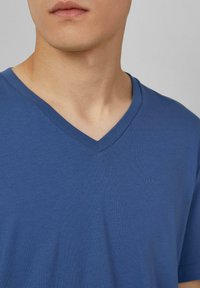 Niebieska koszulka typu V-neck z gładkiego materiału, z subtelnym logo s.Oliver po lewej stronie, dopasowany krój, krótkie rękawy.