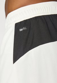 Moške kratke hlače z zgornjim črnim delom in spodnjim belim delom. Narejene so iz zračnega materiala, s črnjenim elastičnim pasom in logotipom "DRYELL".