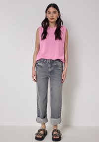 Top rosa senza maniche, jeans grigi a vita alta con risvolti, sandali neri con fibbie decorative e vestibilità dritta.