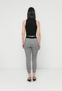 Črn skrajšan top brez rokavov z sivimi karirastimi tights. Tights imajo visok pas in se tesno prilegajo, z gladko teksturo.
