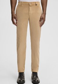 Pantaloni beige in velluto a coste con superficie strutturata, taglio aderente, chiusura con bottoni e orli rifiniti, abbinati a stivali neri in pelle.