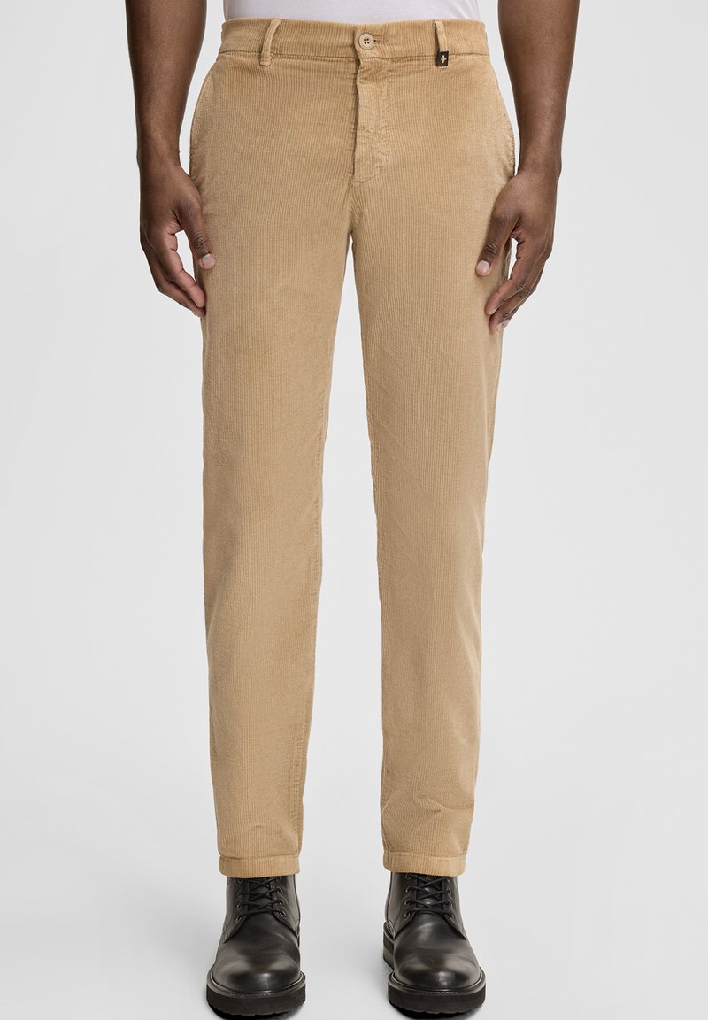 Pantaloni beige in velluto a coste con superficie strutturata, taglio aderente, chiusura con bottoni e orli rifiniti, abbinati a stivali neri in pelle.