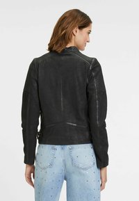 Schwarze Lederjacke mit tailliertem Design, featuring eine glatte Textur und subtile Steppnähte an den Schultern, ergänzt durch seitliche Schnallen.